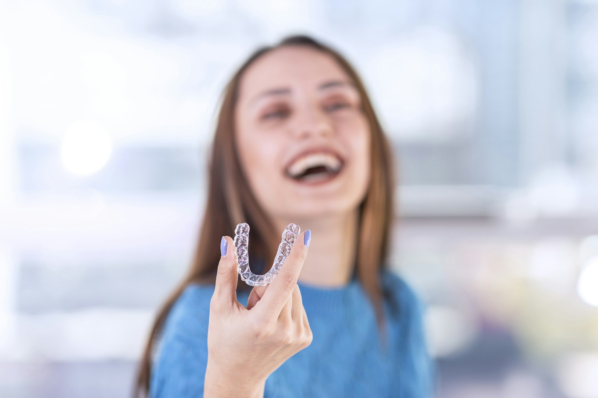 "Woman holding Invisalign aligner, representing FAQs about Invisalign at Wichita Family Dental.
