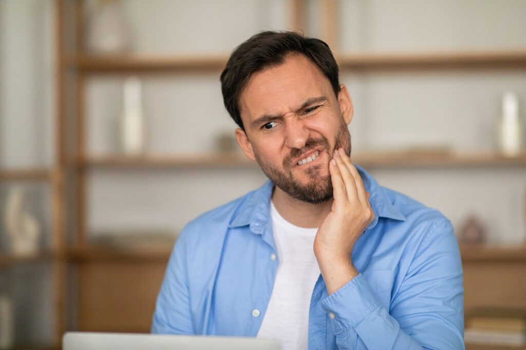 A man rubbing his jaw in pain, experiencing a severe toothache—Wichita Family Dental offers same-day emergency dental care in Wichita to provide fast relief.