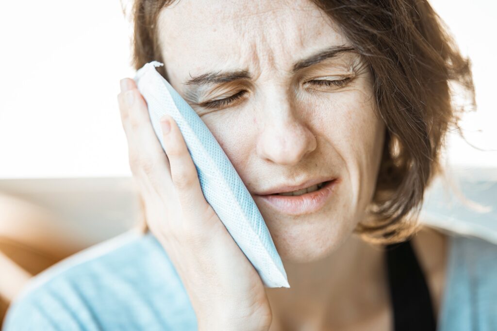Woman applying a cold compress to her cheek to relieve tooth pain.