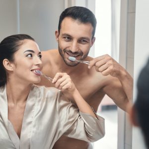 Attractive couple brushing teeth in the mirror, symbolizing the healthy lifestyles supported by Wichita Family Dental.