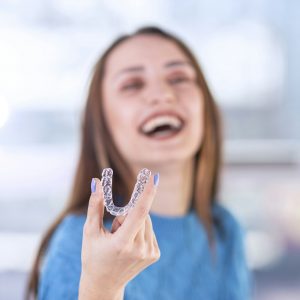 "Woman holding Invisalign aligner, representing FAQs about Invisalign at Wichita Family Dental.